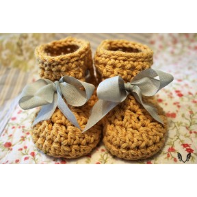 Two yellow baby booties with beige bows sitting on a yellow blanket